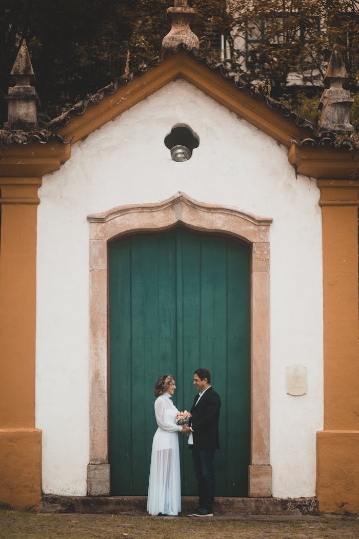 A bride and groom pose romantically in front of a rustic chapel door.